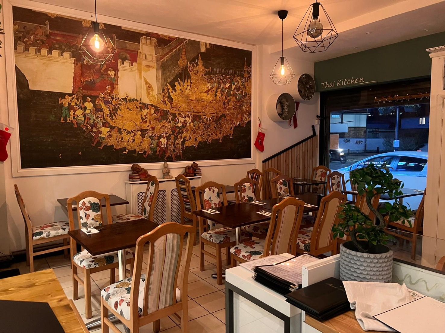 The dining room at Chart Thai — a gold Thai mural along the wall, warm pendant lights and set tables